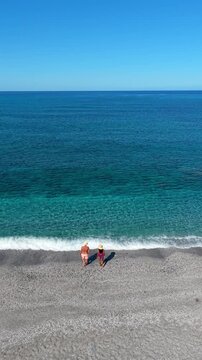 Experience the beauty of La Frana Beach in Sardinia, Italy, with its crystal-clear waters and tranquil atmosphere. A diverse couple of Asian women and caucasian men enjoy a peaceful holiday.