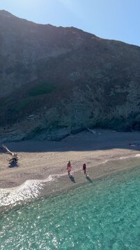 Experience the stunning beauty of La Frana Beach in Sardinia, Italy, with its crystal-clear waters gently lapping against the sandy shore. A diverse couple of Asian women and caucasian men 