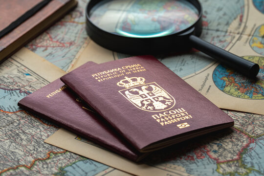 Two Serbian passports displayed with a magnifying glass over vintage maps, symbolizing travel planning, identity verification, citizenship and border crossing.