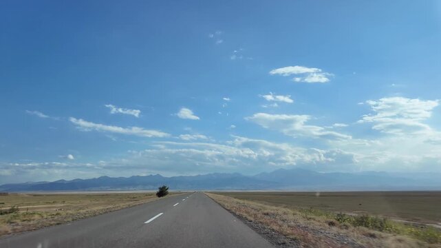 Car driving on endless empty road through vast landscape