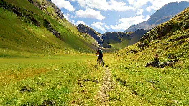 Mountain biker riding on a singletrack trail on a green high plateau in the Alps