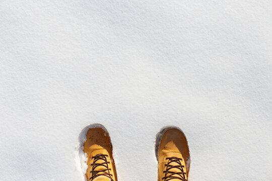 Top-down shot of a person's classic yellow leather hiking or work boots standing on clean, fresh winter snow. Perfect for adventure, cold weather clothing, and outdoor activities concepts.