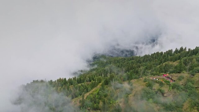 Mount Agung slopes under dense morning mist and clouds, a remote tropical forested mountainside with a small camping settlement tucked into the serene, foggy volcanic landscape. Aerial drone flight