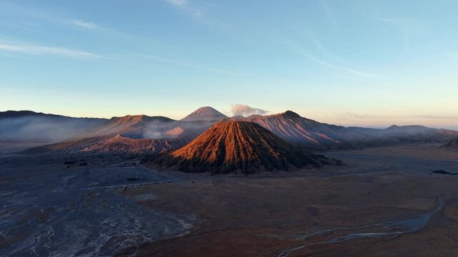 Golden sunrise illuminates Mount Bromo and surrounding volcanic ridges in expansive Tengger caldera aerial view.