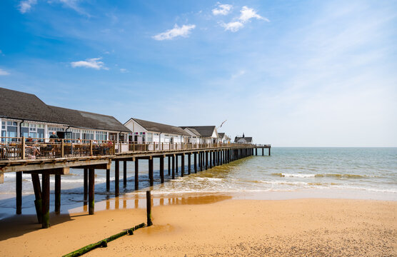 Southwold Pier stretching over the North Sea from a golden sandy beach in Suffolk, England, beneath a bright blue summer sky.