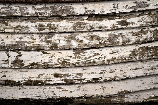 Close-up of peeling white paint and weathered timber on an old wooden boat in Aldeburgh, Suffolk, revealing layers of age, texture and maritime character.