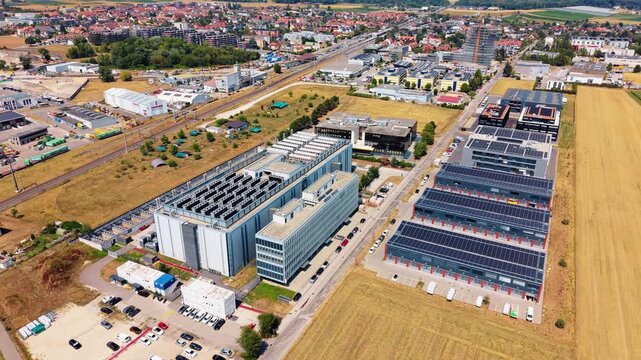 Drone hovers above data center complex beside road town and wheat fields