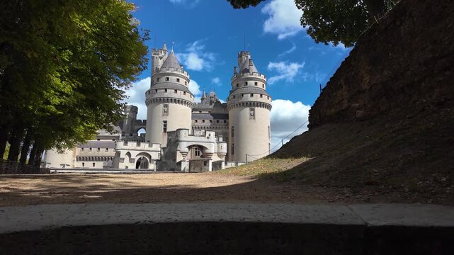 Slow motion pull-up movement reveals Ch&acirc;teau de Pierrefonds between trees and stone walls, highlighting its twin towers, turrets and fortified structure