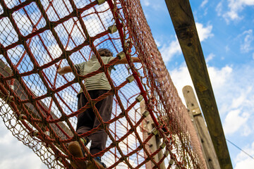 Child climbing through a rope playground structure outdoors, developing balance and coordination while enjoying active childhood play, adventure, movement and exploration © JairoMZ