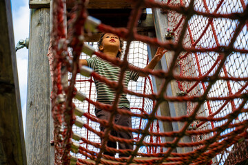 Young child climbing a rope bridge at a playground, photographed from below against the sky, capturing active outdoor recreation, childhood adventure and exploration © JairoMZ