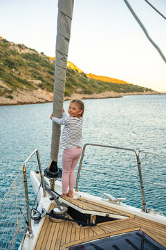 Young girl balancing on bow of sailing yacht near Croatian coast. Childhood adventure at sea represents freedom, confidence, exploration and connection with nature