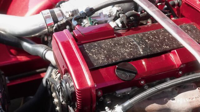 Macro shot of a mechanic&rsquo;s hand checking oil with a dipstick in a polished, turbocharged red car engine bay under natural daylight, highlighting intricate details and focus.