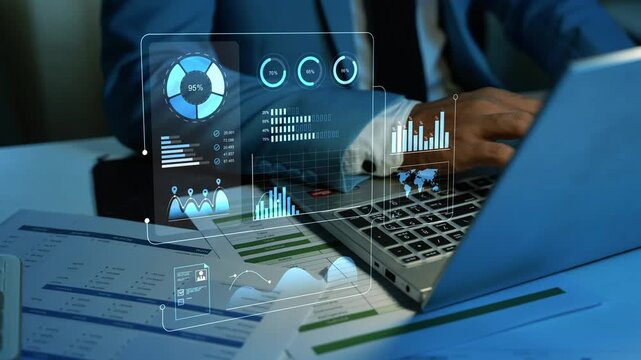 Business professional using a laptop with transparent digital dashboards, charts and financial reports on a desk, showing data analysis and modern office technology.