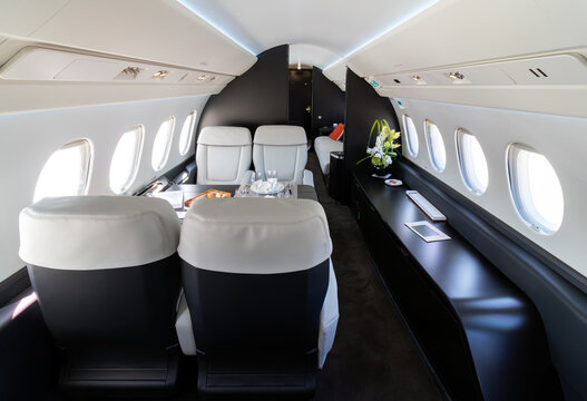 Modern business jet aircraft cabin interior featuring a predominantly white and black color scheme, with leather seating and a contemporary cabin design.