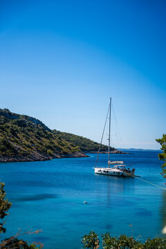 Sailboat anchored in a tranquil bay surrounded by lush green hills and clear blue waters under a bright sunny sky in Solta island, Croatia