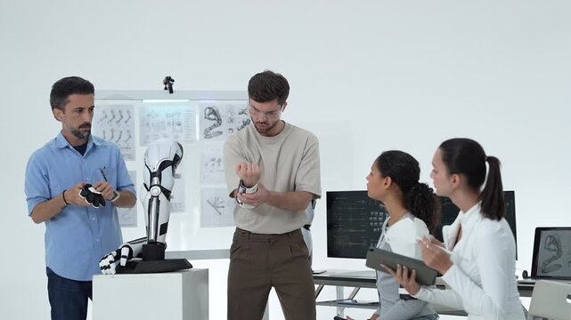 Engineer in safety goggles reacts with surprise while testing a robotic wrist on a volunteer, colleague adjusts the humanoid arm model in the lab