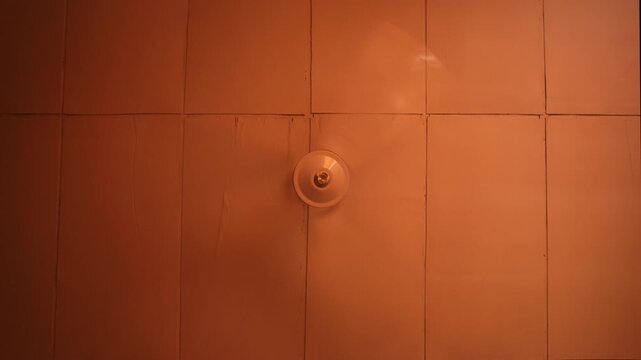 Small circular wall ceiling fan fixture mounted at the intersection of orange rectangular tiles