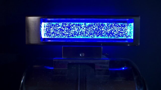 A futuristic cyber punk power-core device glows with intense blue light as shimmering particles and bubbling energy move inside its illuminated chamber.