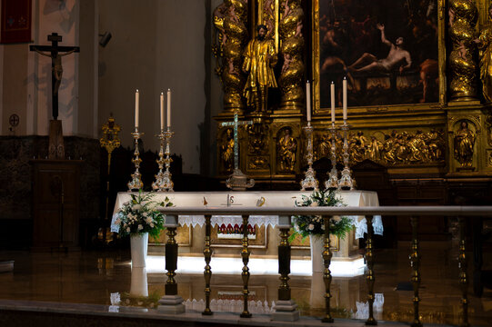  Catholic church altar decorated with white flowers, tall candles, and ornate golden retable.