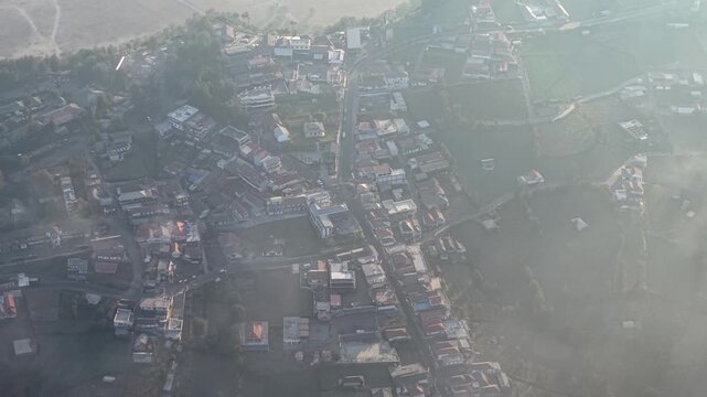Hazy aerial panorama of small mountain village with roads rooftops terraces at sunrise.