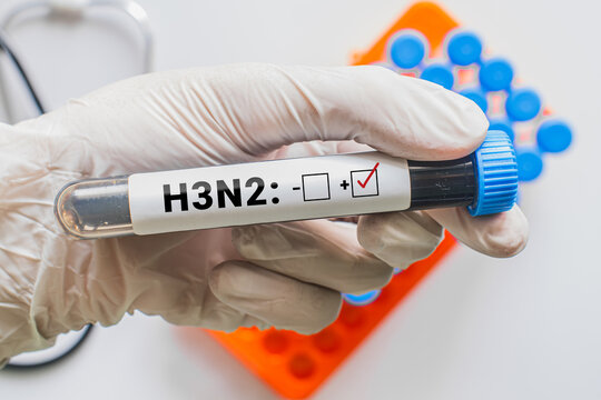 Gloved hand holding H3N2 positive test blood tube with laboratory rack