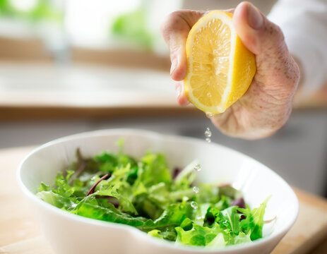 Hand squeezing lemon over fresh green salad