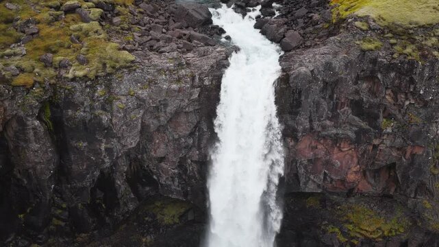 Aerial drone footage of H&aelig;nubrekkufoss Waterfall on the Berufjar&eth;ar&aacute; River, East Iceland, approaching the falls, flying overhead and following the dramatic cascades.
