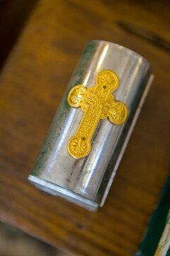 Small silver container with a gold cross design placed on a wooden surface