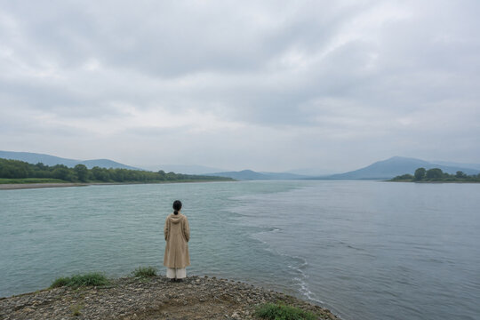 Person in raincoat at river confluence, solitude and nature landscape