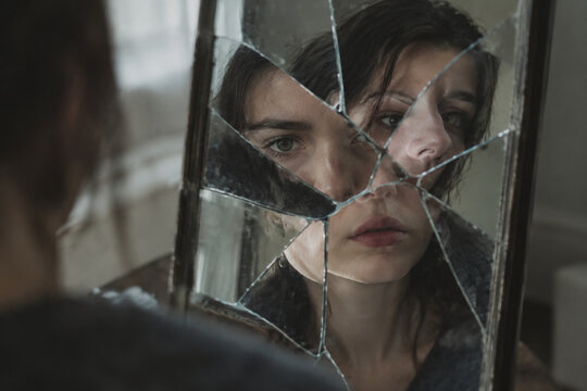 Shattered mirror reflecting fragmented facial features with soft window lighting.