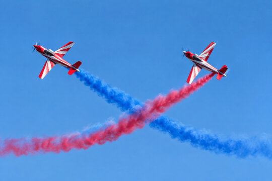 Two red and white stunt planes flying in formation with colored smoke trails.