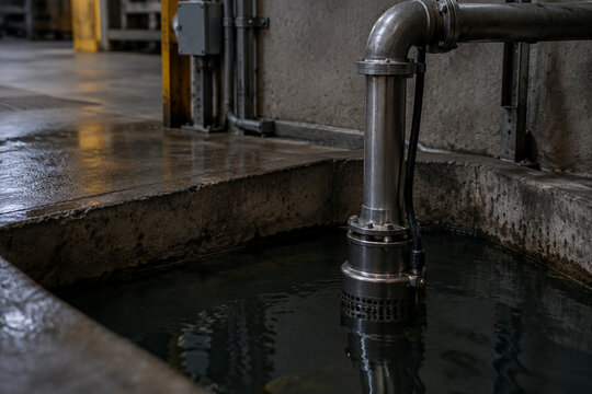 Industrial sump pit with a metal pipe submerged in dark water.