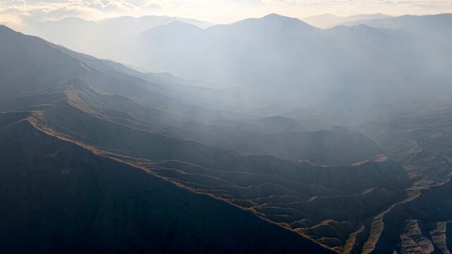 Drone aerial of layered volcanic ridges veiled in soft morning mist at Mount Bromo.