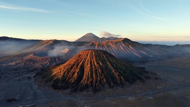 Sunlight bathes volcanic peaks in warm hues. Smoke curls from crater mouths at Mount Batok, Bromo.