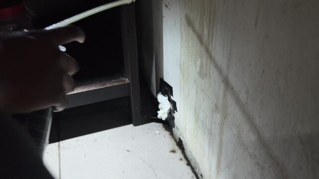 Medium shot of filling wall corner hole with expanding polyurethane foam spray for pest control and home repair
