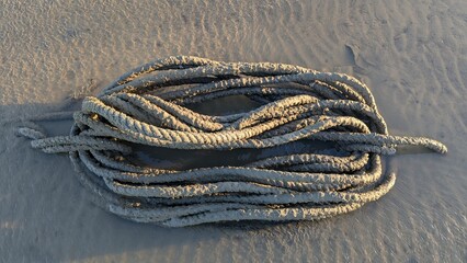 Coiled white boat mooring rope covered in muddy sand at low tide beach © Arid Rahman