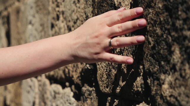 Close-up of a hand touching the rough textured surface of an old stone wall, highlighting natural stone texture and tactile interaction.