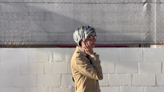 Mujer +50 caminando por zona urbana con auricular inal&aacute;mbrico