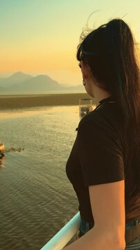 Woman tourist on excursion stands on boat enjoying view Lake Skadar on Balkan, Montenegro, Albania. green plants leaves specifically water caltrop, Trapa natans, float cover water surface. Sunset sky 