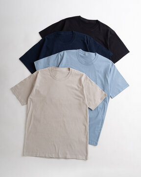 Flat lay composition of four blank cotton t-shirts in beige light blue navy blue and black colors on a white background