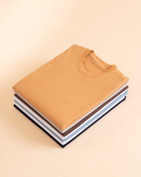 A stack of neatly folded colorful cotton t shirts arranged on a matching beige background