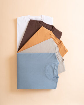 A vertical stack of colorful folded cotton t shirts arranged on a neutral beige background