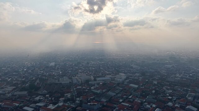 Sunbeams pierce hazy sky above sprawling urban sprawl at Surabaya old town