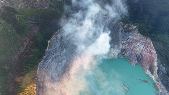 High altitude drone shot of steaming Mount Ijen crater with turquoise acidic lake and rugged volcanic rim.