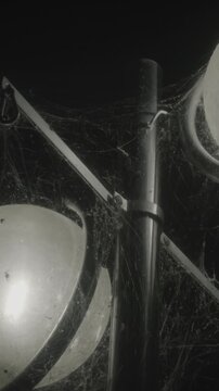 Dust-covered lamp globe and pole draped in thick cobwebs with tiny spiders glow in the dark, eerie vertical close-up made for Halloween reels, horror shorts and stories.