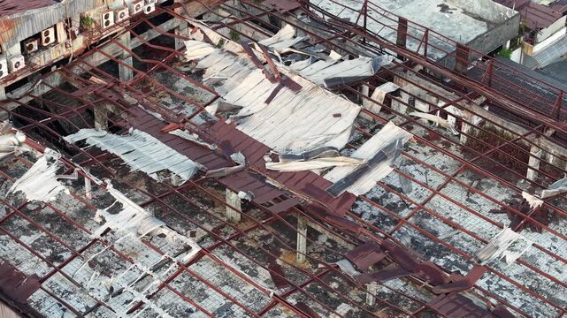Broken metal roof lies in ruins. Red rusted beams crumble under white tattered layers