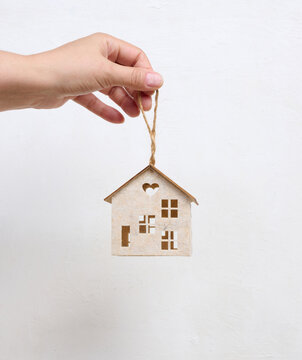 Person holding a small wooden house model on their palm against a light background.