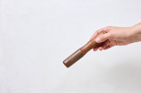 A person holding a wooden singing bowl pestle in their hand