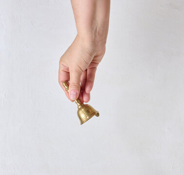 A person holding a small brass bell in their hand against a light background.
