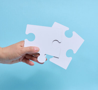 Hand holding a single white puzzle piece against a blue background